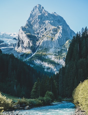 river flowing through a lush dense forest with towering mountains in the background